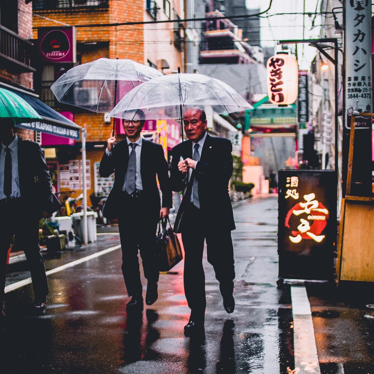 two men in black suit holding transparent umbrellas walking in the street